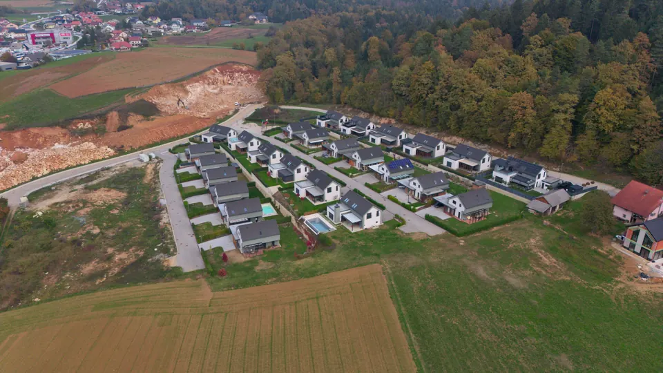 Novo naselje ob robu gozda med obdelanimi polji, v ozadju bližnji kraj, posneto z dronom poševno s strani