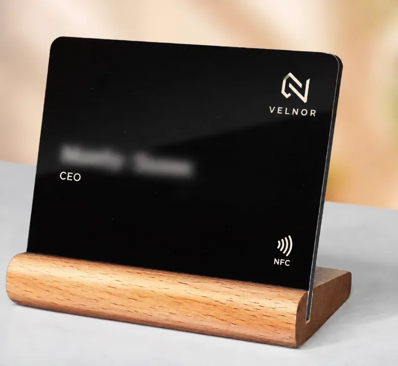 Črna NFC vizitka Velnor z logotipom, nazivom CEO in NFC znakom v leseni podstavki na mizi